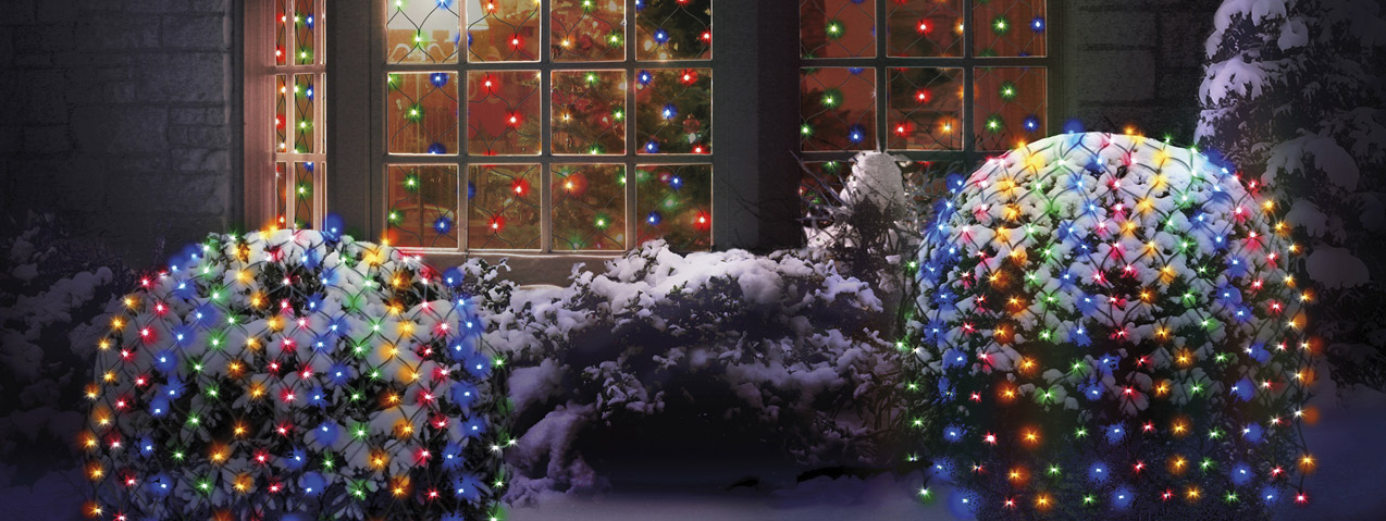 LED multicoloured lights on hedges and inside winder of snowy house